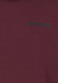 Burgunder Baumwollstoff T-Shirt mit einem schwarzen bedruckten "WORLDWIDE"-Text in einer einfachen serifenlosen Schriftart, der auf der Vorderseite positioniert ist.