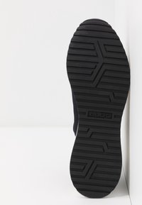 Semelle de chaussure en caoutchouc noir avec un motif géométrique de la bande de roulement et le nom de la marque "ALDO" embossé au centre sur fond blanc.