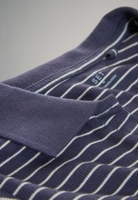 Navy blue polo shirt with white horizontal stripes, ribbed collar, and button. Cotton material with smooth texture and clean stitching details.