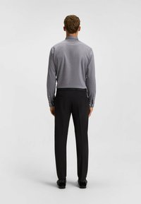 Camicia grigia a maniche lunghe con colletto, abbinata a pantaloni neri. La camicia presenta bottoni sui polsini e una texture liscia.