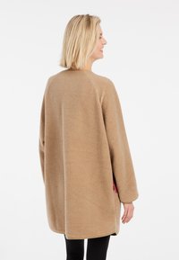 Beige fleecejack met lange mouwen, raglanontwerp en een zachte textuur. Heeft zijzakken en een afgeronde zoom.