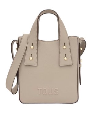 Bolso de mano de piel beige con asas dobles, correa de hombro ajustable, tachuelas doradas y logotipo "TOUS" en relieve en la parte delantera.