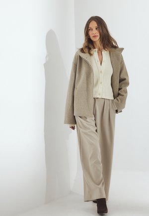 Bežový oversize kabát z vlnenej zmesi, krémový pletený sveter s gombíkmi a bežové široké nohavice. Textúrovaná tkanina, minimalistický dizajn.