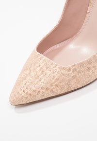 Vaaleanpunainen kuvioitu korkokenkä, jossa on terävä kärki, sileä sisävuori ja kankaan hienovarainen hohto.