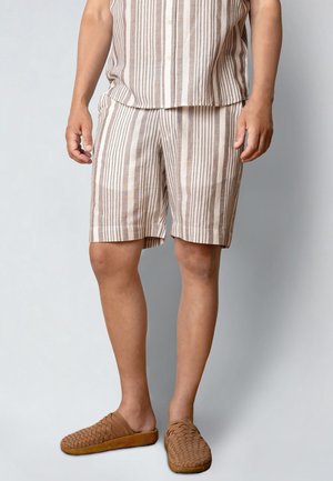 Lekki beżowy zestaw koszula i szorty w paski, z poziomymi i pionowymi paskami. Do kompletu brązowe, plecione buty wsuwane.