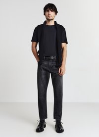 Maglietta nera sotto un maglione nero senza maniche, abbinata a jeans neri a vita alta e gamba dritta e scarpe nere con stringhe.