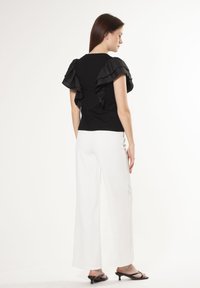 Top negro con mangas acampanadas, parte delantera lisa, silueta ajustada. Combinado con pantalones blancos de pierna ancha y zapatos negros de tacón abierto. Diseño simple y elegante.