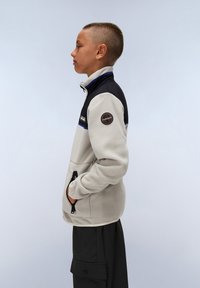 Fleecejacka i beige med svarta detaljer, hög krage, blå sömmar och en logopatch. Har sidfickor och en avslappnad passform.