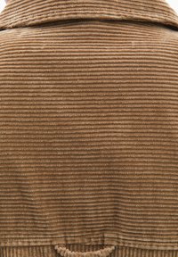 Tessuto in velluto a coste marrone con texture a coste e collo visibile. Presenta un anello all'orlo inferiore per appendere o riporre.