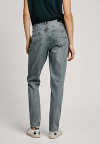 Jeans de tiro alto en gris con corte recto, lavado desvaído, bolsillos visibles y una etiqueta en la cinturilla, combinados con zapatillas plateadas brillantes.