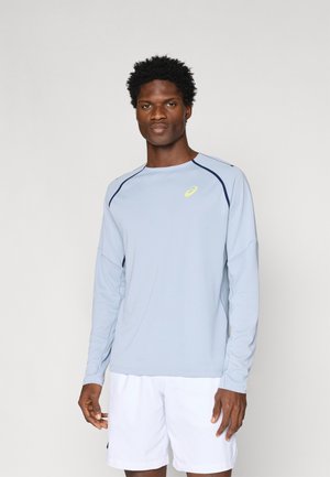 Hele sinine pikakäisteline särk tumesiniste aktsentidega, ümar kaelus ja logo rinnal. Valmistatud siledast ja hingavast kangast. Kantud valgete lühikeste pükstega.