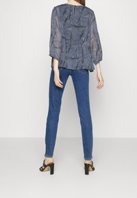 Sheer navy blouse with wavy line pattern, balloon sleeves, and back zipper, paired with fitted blue jeans and black block-heel sandals.
