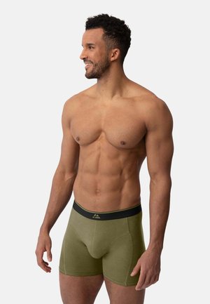 Olivgrüne Boxershorts mit einem schwarzen Bund, die eine glatte Textur und ein anschmiegsames Design aufweisen, das eine konturierte Tasche betont.