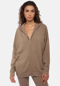 Hoodie marron à fermeture éclair avec une coupe décontractée, tissu texturé et capuche à cordon. Comprend une fermeture éclair intégrale et des accents côtelés aux poignets.