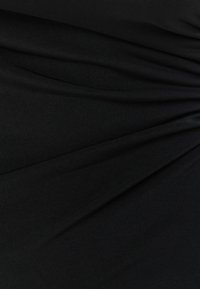 Svart tyg med en slät yta, försett med hopdragna veck som skapar en draperad look. Inga tydliga mönster eller hårdvara synliga.