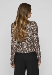 Halenka s dlouhými rukávy v hnědém a béžovém leopardím vzoru, měkká tkanina, upnutý střih a kulatý výstřih. Spárováno s černými kalhotami.