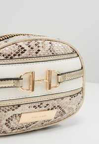 Petit sac à main beige à motif peau de serpent, détail boucle dorée et plaque avec le logo River Island.
