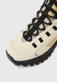 Tan- och krämfärgade sneakers med ett svart snörningssystem, som har nätpaneler, texturerade överdrag och en robust svart sula.
