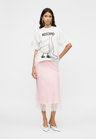 Λευκό υπερμεγέθες t-shirt με γραφικό παπάκι και εκτύπωση "Moschino", συνδυασμένο με ροζ σατέν φούστα με φάσα δαντέλας και λευκά μυτερά τακούνια.