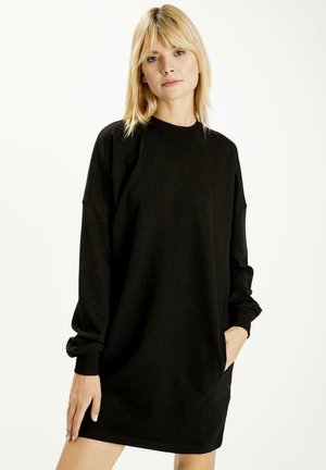 Czarna, oversize sukienka-sweterek, z długimi rękawami i marszczonymi mankietami, z prążkowanym dekoltem, kieszeniami po bokach, w casualowym i miękkim materiale.