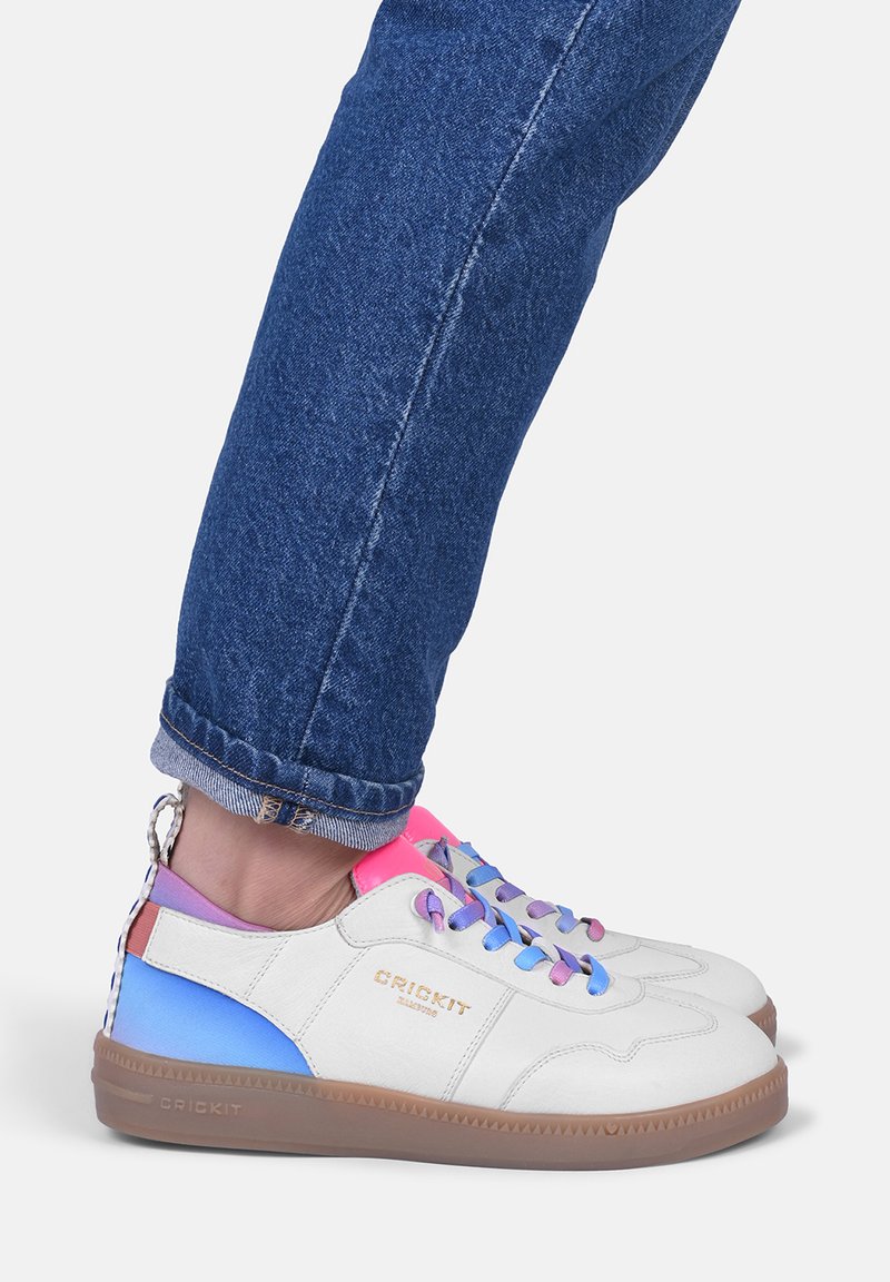 Sneakers bianchi con dettagli multicolore in rosa, blu e viola. Presentano una suola in gomma neutra, chiusura con lacci e un logo sul lato.