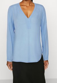 Blusa azzurro chiaro a maniche lunghe con scollo a V, caratterizzata da una texture sottile e orlo dritto, abbinata a una gonna nera.