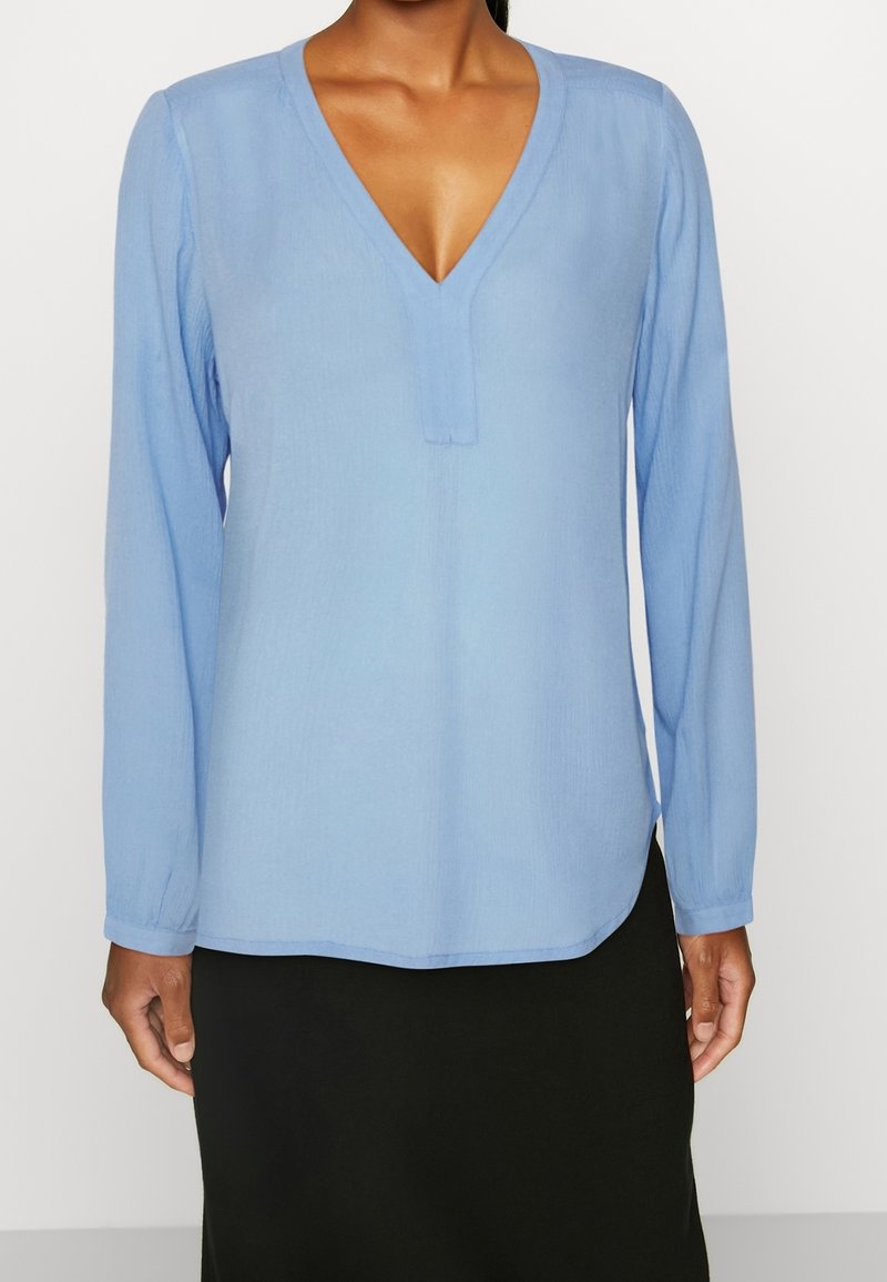 Blusa azzurro chiaro a maniche lunghe con scollo a V, caratterizzata da una texture sottile e orlo dritto, abbinata a una gonna nera.