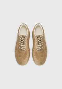 Baskets en suede beige avec des lacets blancs, bout rond et col rembourré. Présente une tige texturée et une semelle en caoutchouc beige clair lisse.