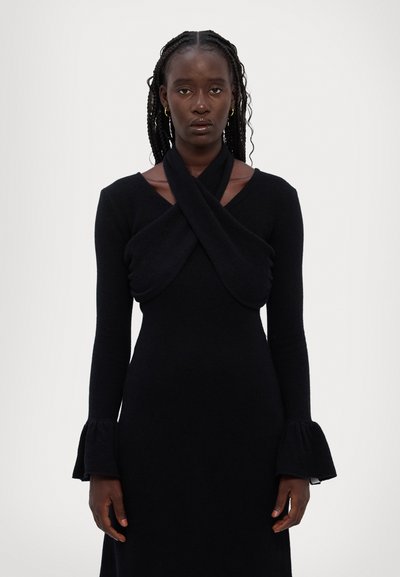 Robe noire à manches longues dotée d'un décolleté torsadé et de poignets évasés, réalisée en un tissu doux et texturé. Design minimaliste avec une finition lisse.