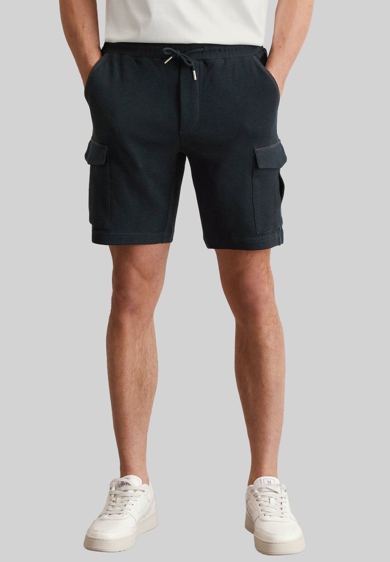 Shorts cargo bleu foncé avec taille à cordon, deux poches latérales et tissu texturé. Associés à des baskets blanches.