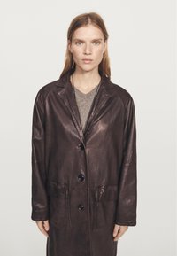 Bruine leren jas met een notch-rever, voorste knoopsluiting en twee opgestikte zakken. De textuur is glad met een subtiele glans.
