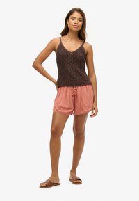 Top de punto marrón sin mangas con escote en V y tirantes de espagueti, combinado con pantalones cortos sueltos en color coral con una cinturilla elástica y bolsillos laterales.