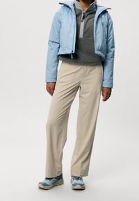 Ljusblå kort jacka, grå fleecepullover, beige byxor och gråblå vandringsskor. Släta texturer och praktisk design.