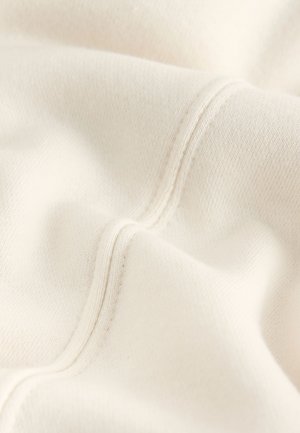 Kremasti pamučni materijal s mekim teksturom, s vidljivim šavovima i suptilnim varijacijama boje po površini.