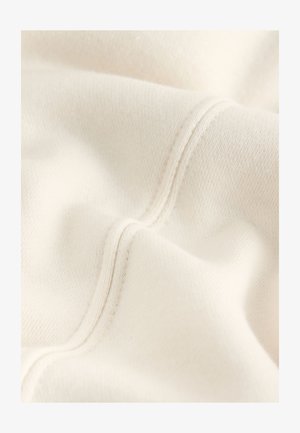 Crèmekleurige katoenen stof met een zachte textuur, met zichtbare stiknaden en subtiele kleurvariaties over het oppervlak.