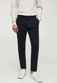 Pantalons ajustés bleu marine en tissu sergé de coton, présentant une coupe slim et des poches latérales, associés à des baskets blanches.