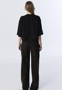 Top nero in tessuto texturizzato con rouches a strati, abbinato a pantaloni a gamba larga con stampa leopardata marrone, che mostrano una vestibilità rilassata e in cotone.