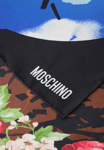 Coin de tissu noir avec texte blanc MOSCHINO superposé à un tissu coloré à motifs floraux et abstraits en bleu, blanc et marron.