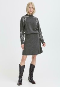 Maglione a maglia grigio scuro con dettagli a motivo foglia sulle maniche, abbinato a una gonna a maglia grigia e stivali da cowboy neri.
