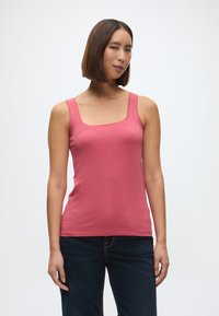 Różowy bawełniany top na ramiączkach z kwadratowym dekoltem i szerokimi ramiączkami, zestawiony z ciemnoniebieskimi dżinsami. Gładka tekstura, dopasowany krój.