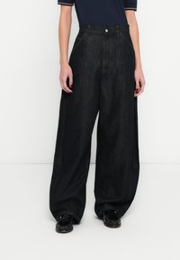 Széles szárú, fekete farmernadrág magas derékkal, finom varrással és strukturált szabással. Fekete mokaszinekkel párosítva a kontraszt érdekében.