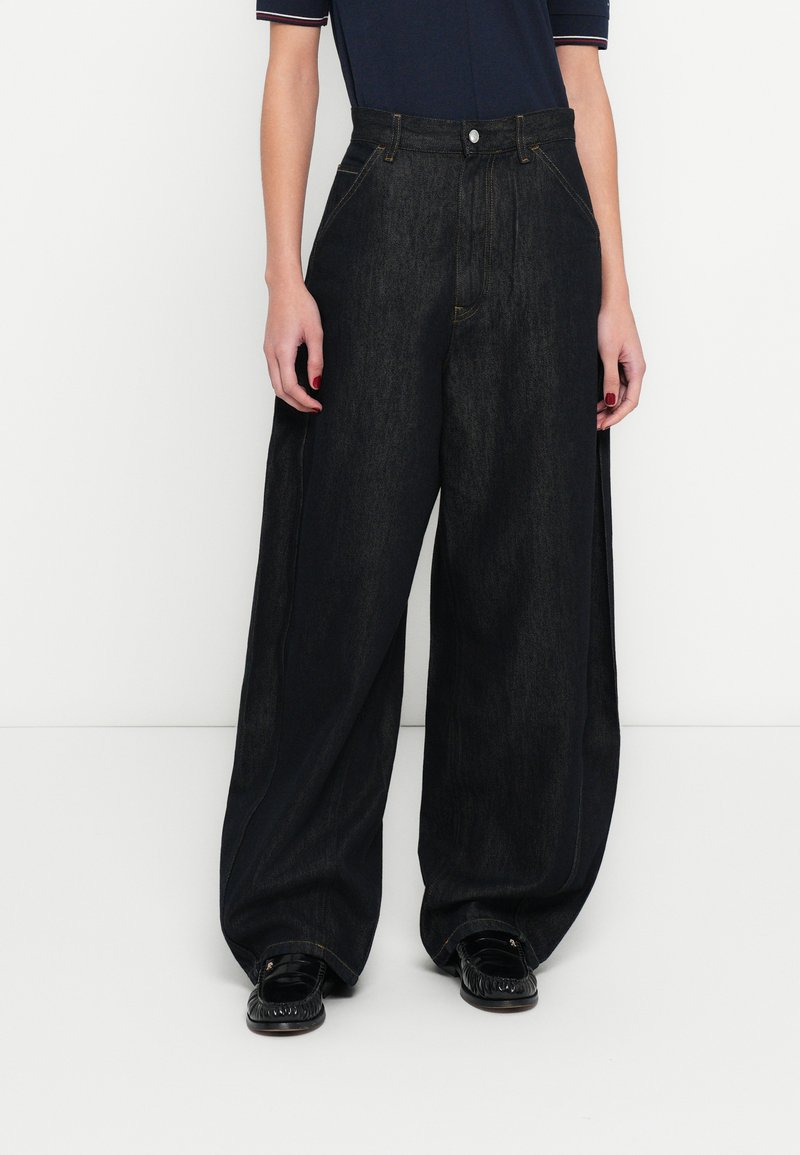 Széles szárú, fekete farmernadrág magas derékkal, finom varrással és strukturált szabással. Fekete mokaszinekkel párosítva a kontraszt érdekében.