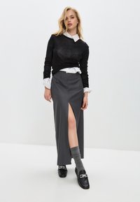 Šedá dlouhá sukně s předním rozparkem, nošená přes bílé tričko a černý svetr. Černé loafers s stříbrným kováním dokončují look.