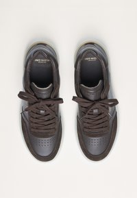 Brown leather sneakers with perforated upper, dark laces, and a translucent sole. Branding visible on the tongue and side accents.