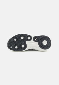 Black rubber sneaker sole with circular patterns and white accents. Features prominent treads and Under Armour logo on the side.