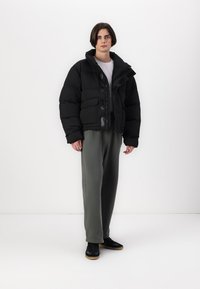 Svart boblejakke med oversized passform, som har store frontlommer, trykknapper og høy krage. Modellen har på seg grå joggebukser og svarte sko.
