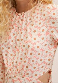 Vestido floral con un fondo rosa, adornado con margaritas blancas y centros marrones. Escote fruncido y cortes laterales para un detalle adicional.