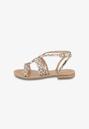 Sandal de punta abierta con cintas metálicas trenzadas, plantilla en color beige neutro, suela plana y hebilla ajustable en el tobillo para un ajuste seguro.