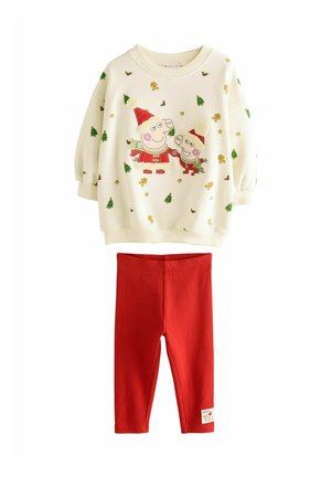 Kinderoutfit mit einem cremefarbenen Pullover, der festliche Charakterdrucke und grüne Baumakzente aufweist, kombiniert mit roten gerippten Leggings.