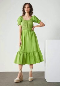 Vestido midi de algodão verde com mangas bufantes, bainha com folhos em camadas e detalhes franzidos no corpete. Combinado com cunhas de espadrille bege.